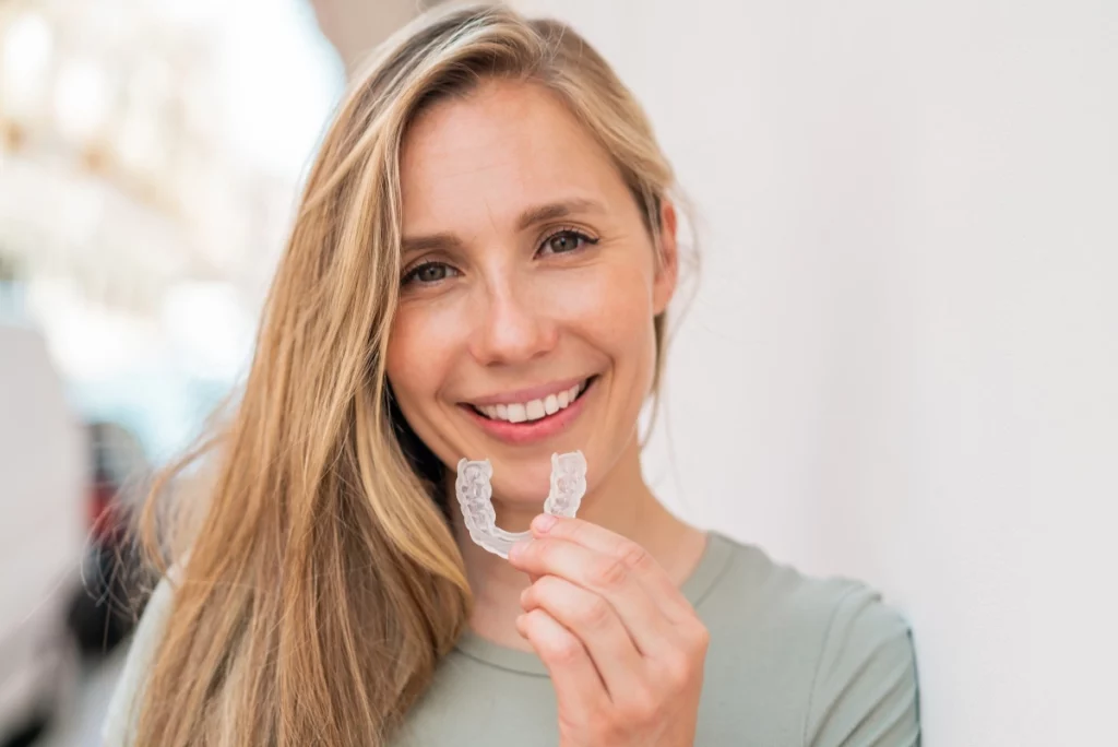 Blonde Frau hält transparente Zahnschiene in Hand